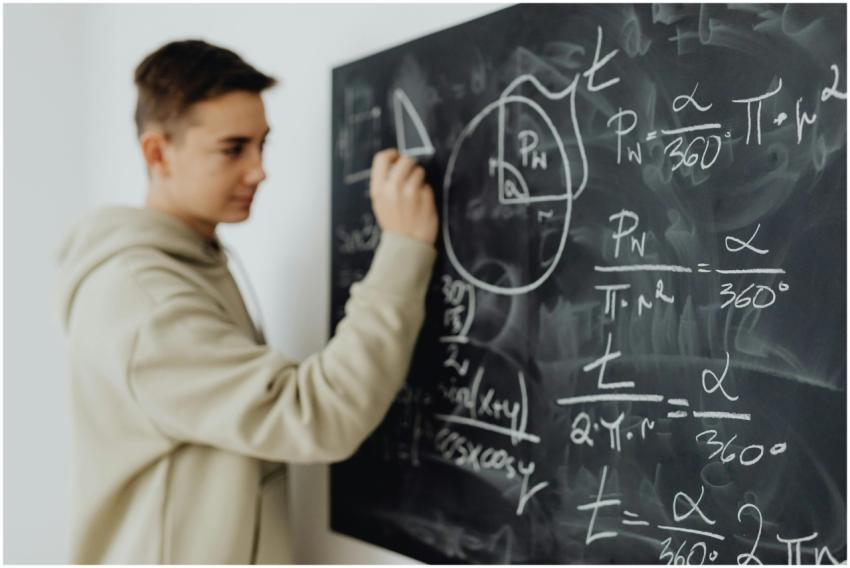 Focused teenager solving a math equation on a blac