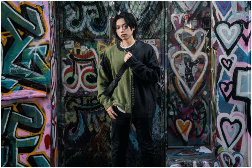 A stylish young adult poses against vibrant graffi