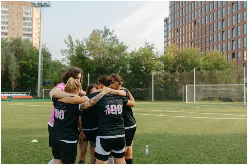 Women's football team huddles on a city field, emp