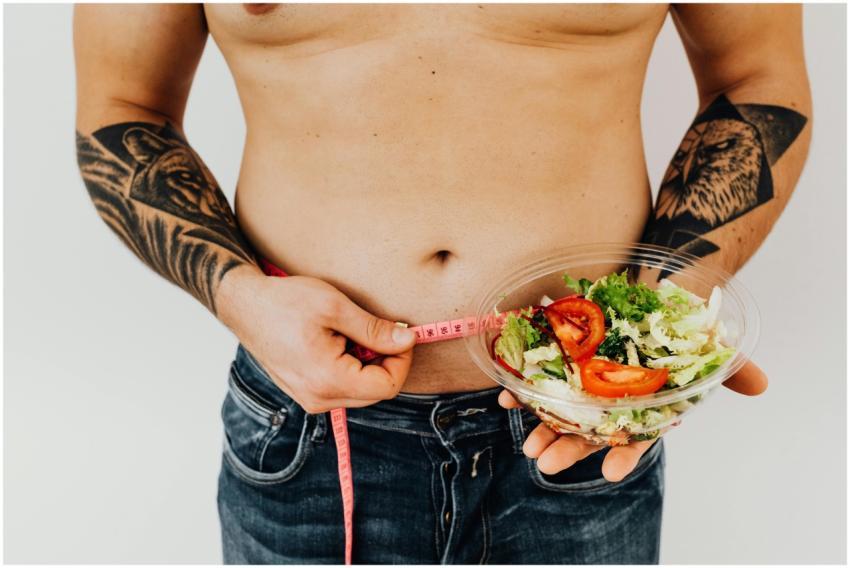 Tattooed man measuring waist while holding fresh s