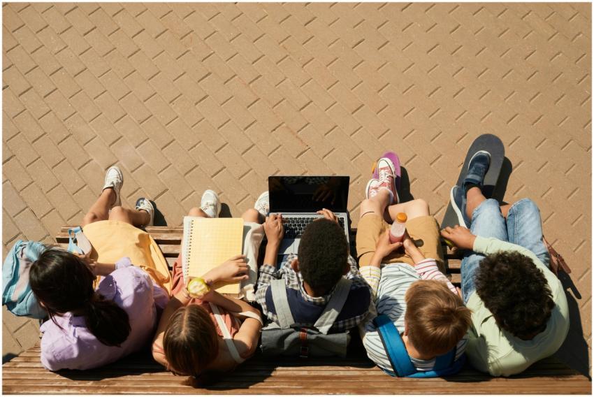 Group of teenagers sitting on a bench with a lapto