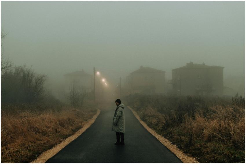 Person stands on a foggy, dimly lit street with di