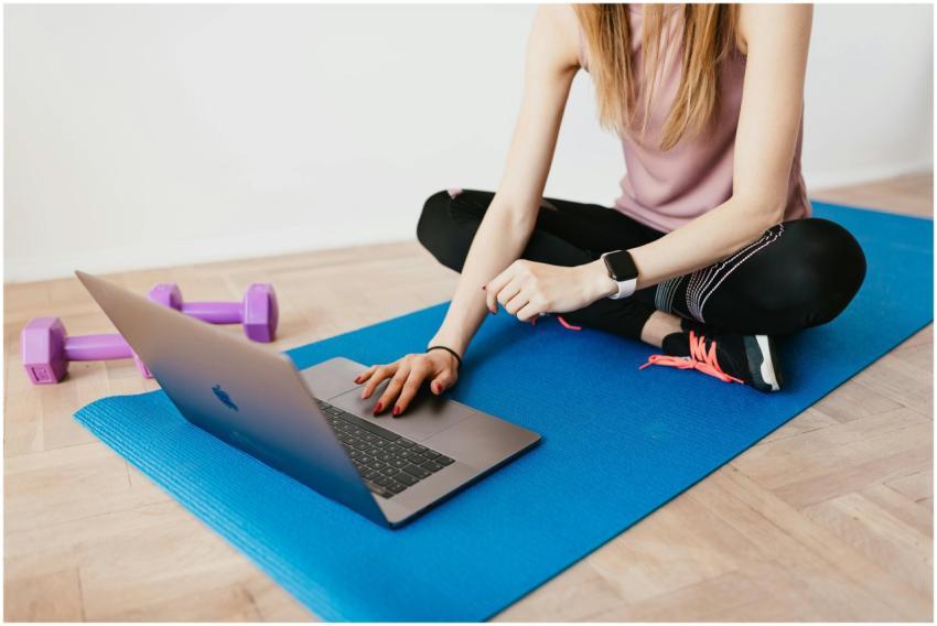 Woman in activewear using a laptop on a yoga mat w
