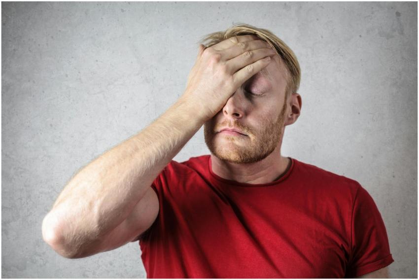A frustrated man in a red shirt holds his head in