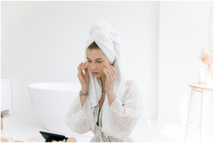 Woman in white bathrobe applying skincare in a bri