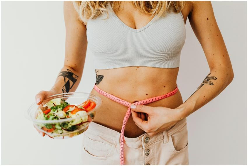 Woman measuring waistline while holding a fresh ve
