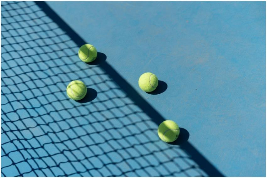 Four tennis balls resting on a blue tennis court w