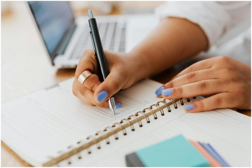 Woman with blue nails writing in a spiral notebook