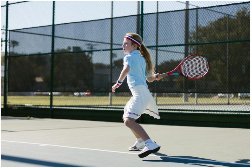 A young girl actively playing tennis on an outdoor