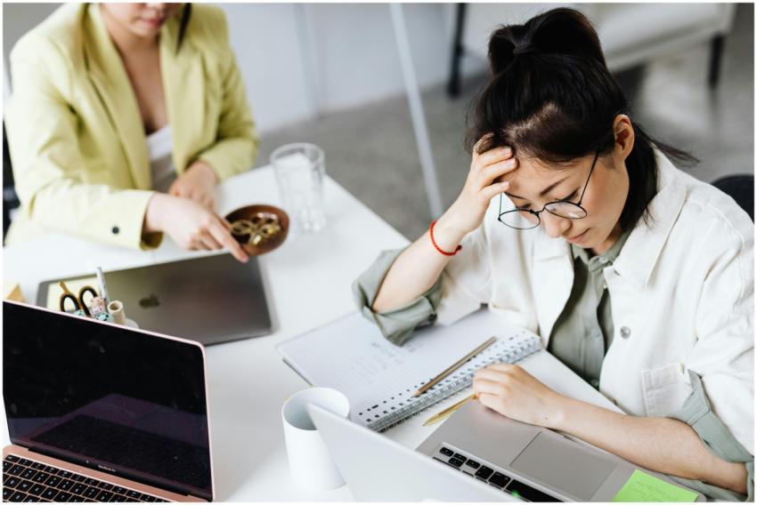 A woman in glasses stressed over work at a laptop,