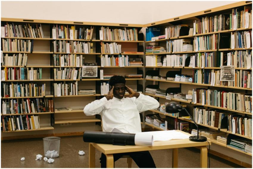 A student seated at a desk in a library, surrounde