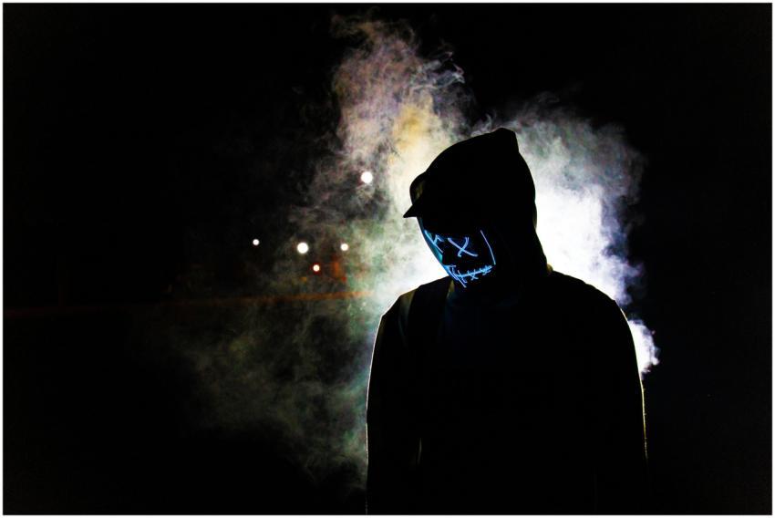 A man in a hooded sweater wears a glowing LED mask
