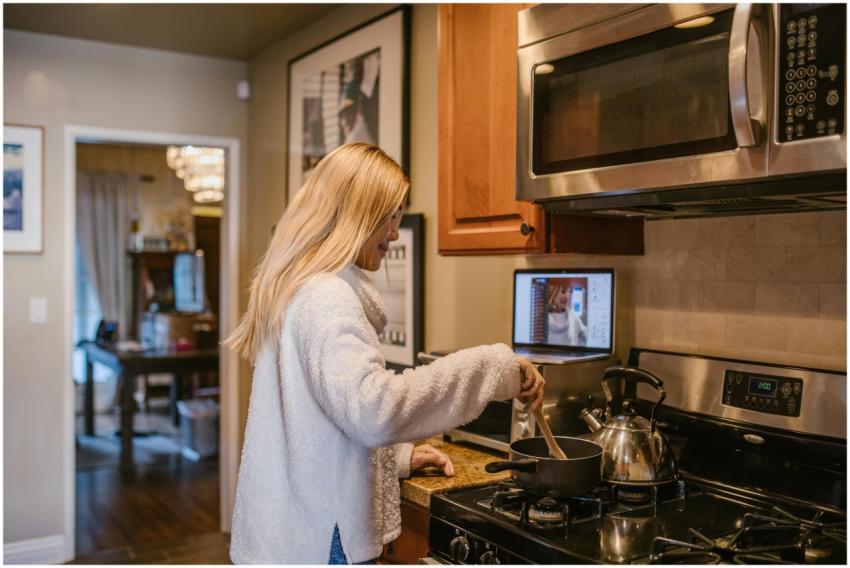 A woman cooks while attending an online class from