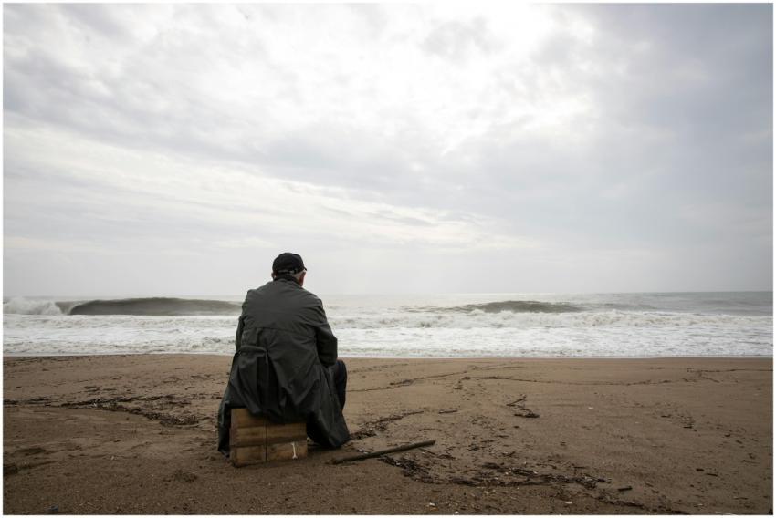 A man sitting alone on an empty beach looking at t