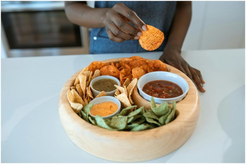 A hand picks a spicy chip from a wooden platter wi