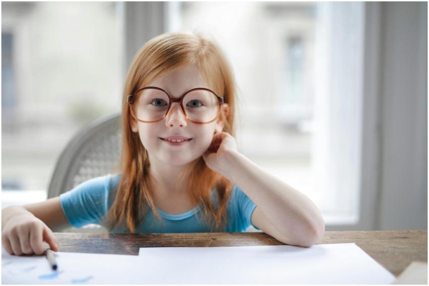 Smiling girl wearing eyeglasses, sitting indoors a