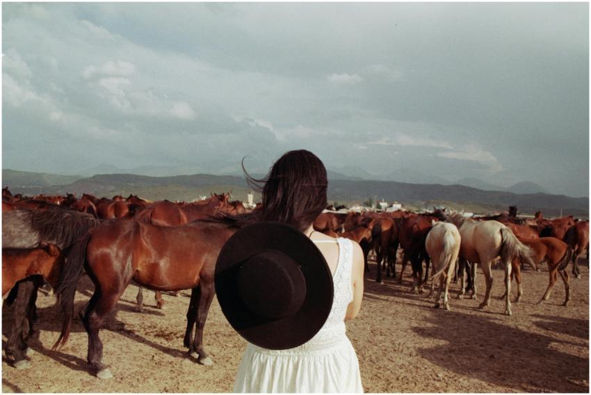 A woman in a white dress and hat stands with her b