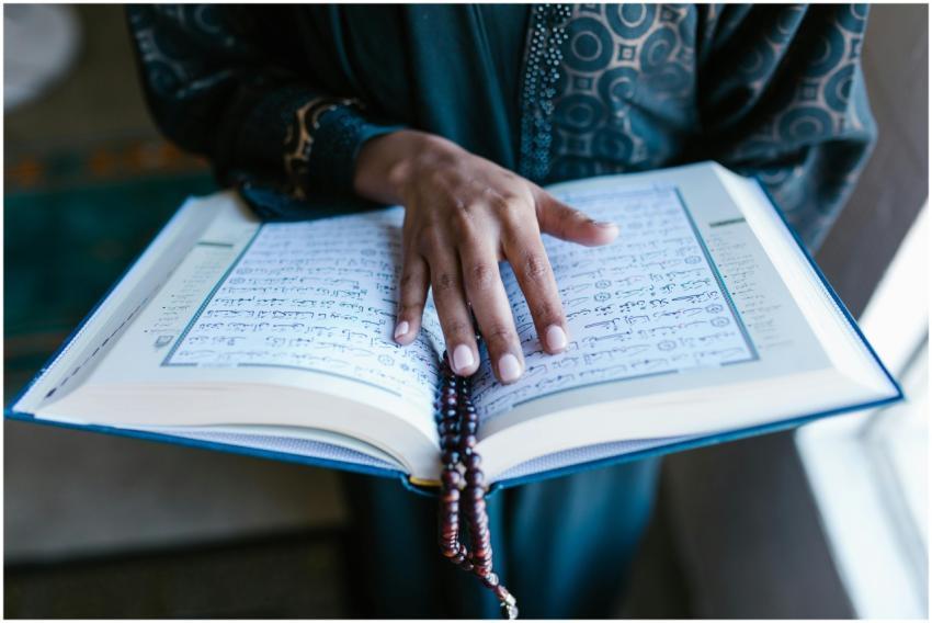 A woman's hand rests on an open Quran with prayer