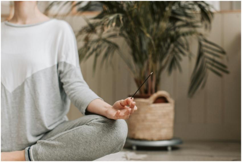 Woman meditating indoors holding incense, promotin