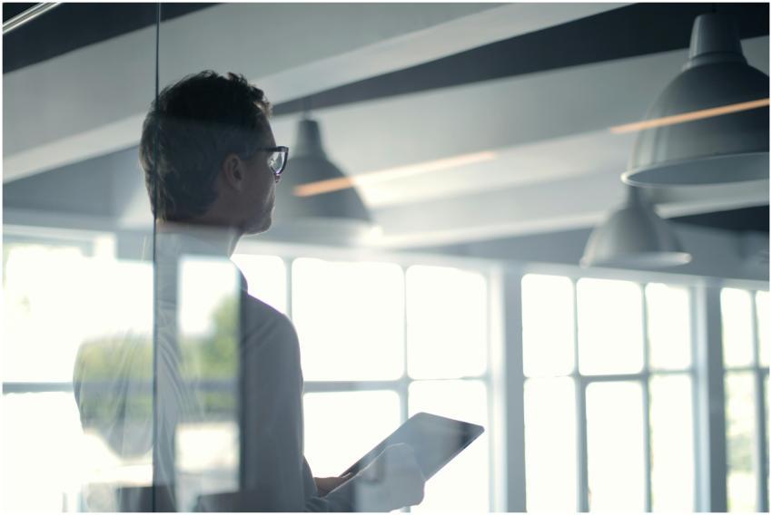 A businessman holding a tablet in an office, looki
