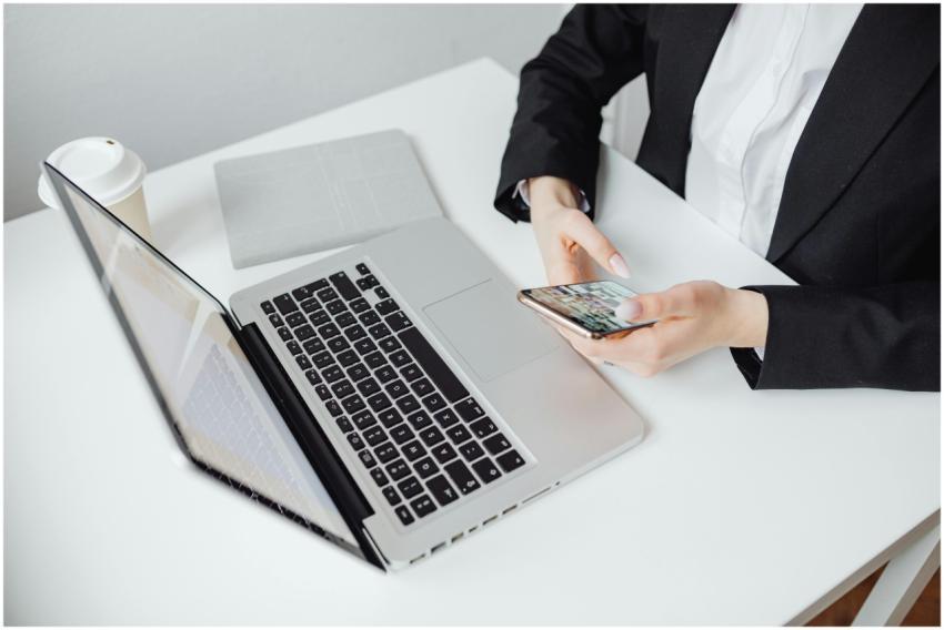 Businesswoman using smartphone at desk with laptop