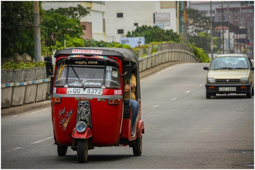 Red tuk-tuk taxi driving on an urban road, showcas