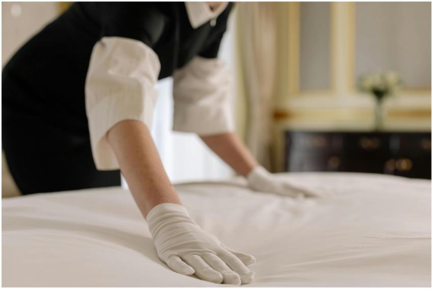 A housekeeper straightening the bed linens in a we