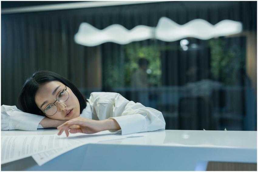 Asian woman in glasses rests her head on a counter