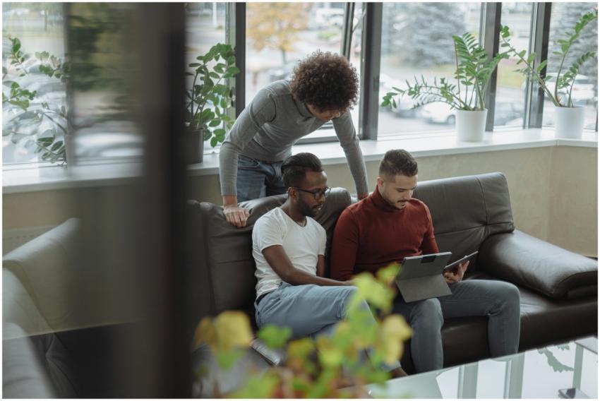 Three men discuss projects using a tablet in a bri