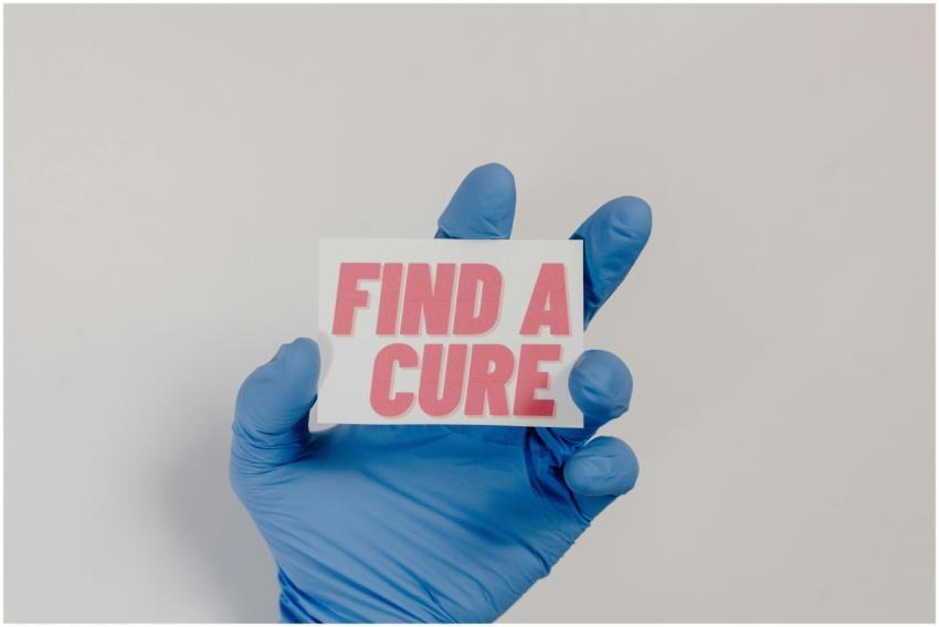 A blue-gloved hand holds a card with 'Find a Cure'