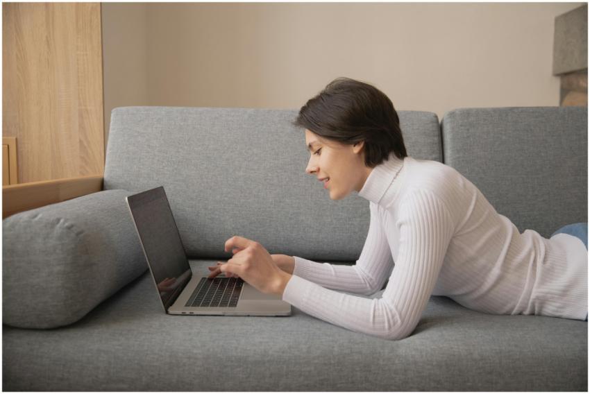 Woman lying on a sofa at home working remotely on