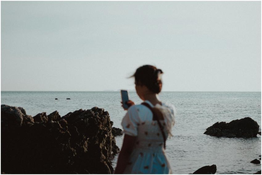 A woman stands by a rocky seaside, capturing the m