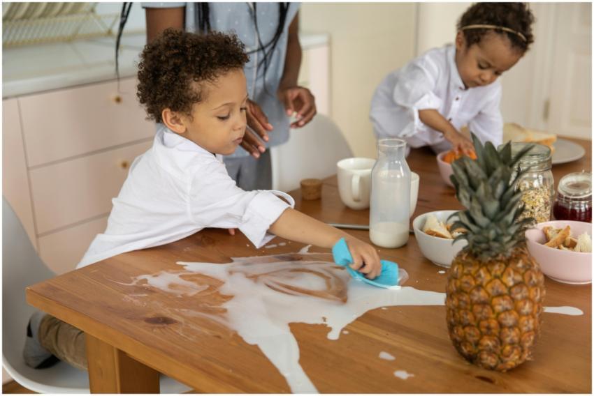Children clean up a milk spill on a wooden breakfa