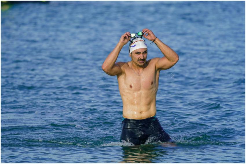 A male swimmer with goggles and swim cap emerges f