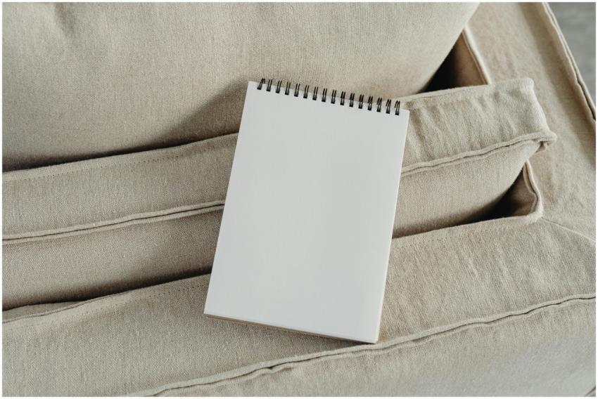 A blank spiral notepad placed on a beige sofa, per