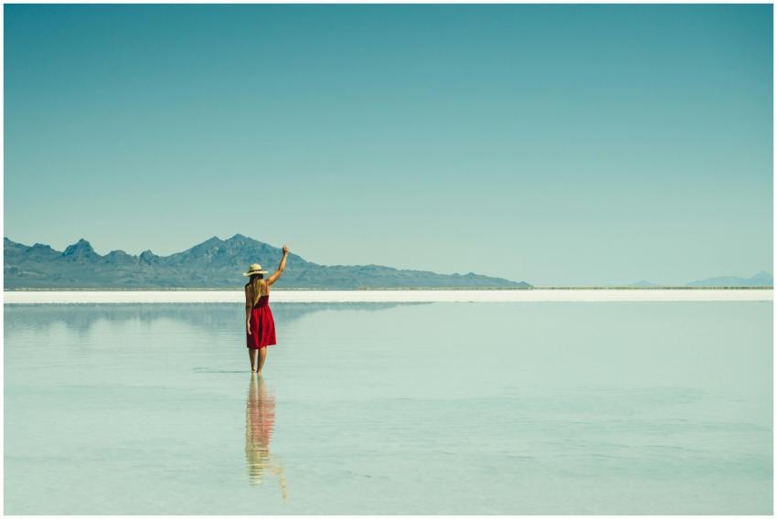 A woman in a red dress stands at a serene salt fla
