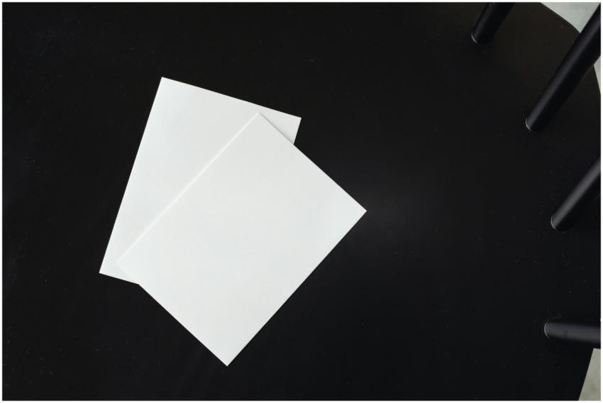 Two blank white paper sheets on a black surface, s