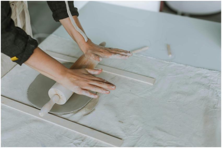 Hands rolling clay for pottery on a workbench with