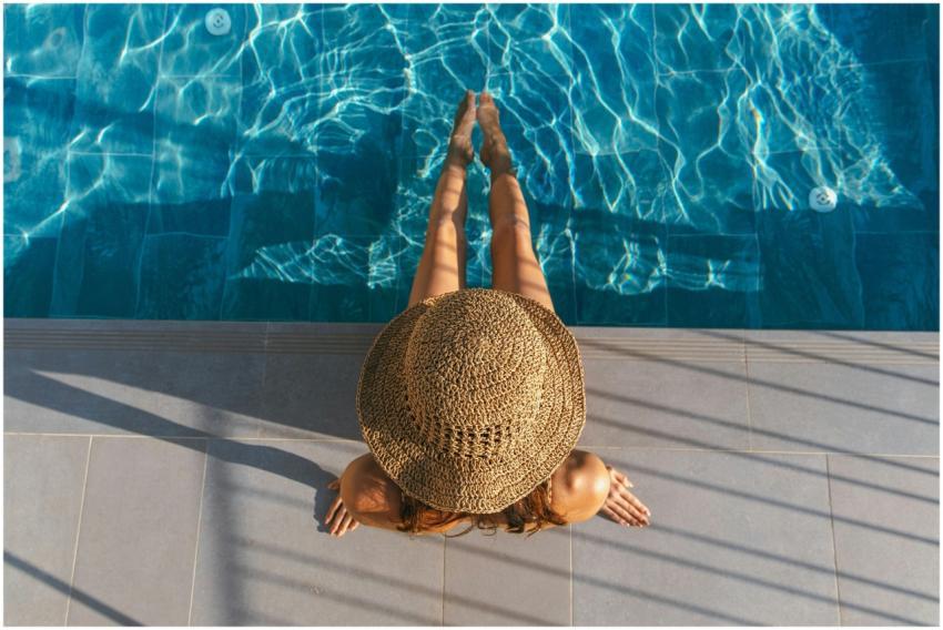 An adult woman in a sunhat relaxes poolside, enjoy