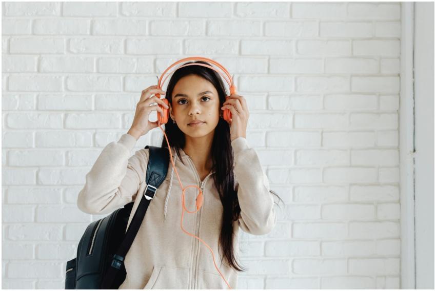 Teen girl wearing headphones and a backpack agains