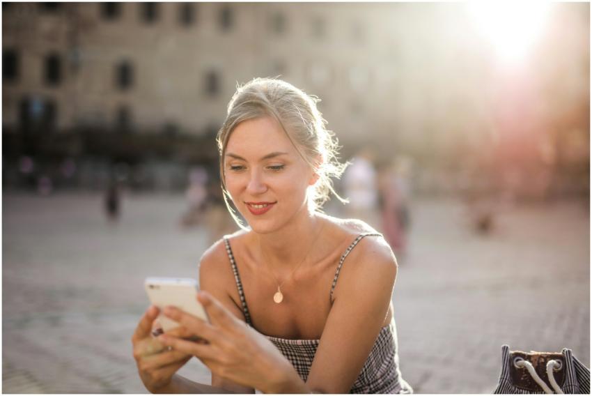 Smiling woman using smartphone outdoors in city sq