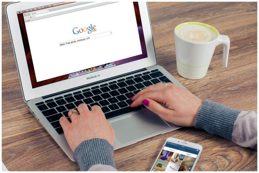 Hands typing on MacBook Air with Google search ope