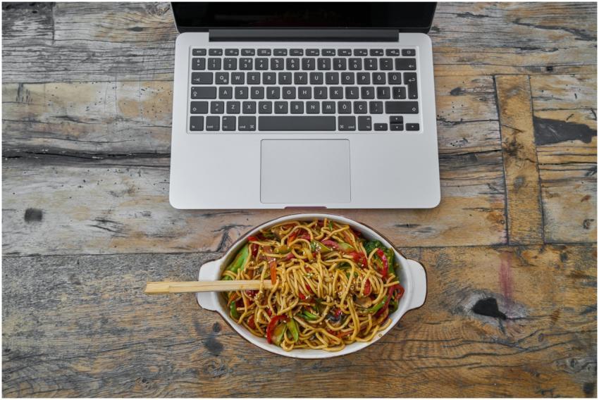 Overhead view of laptop and noodle bowl on rustic
