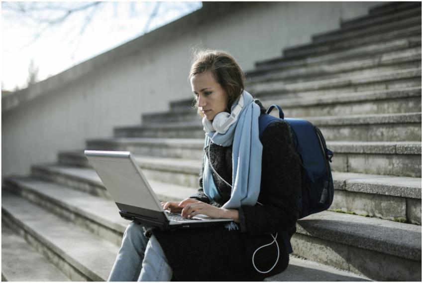 Woman using laptop on outdoor stairs, studying onl