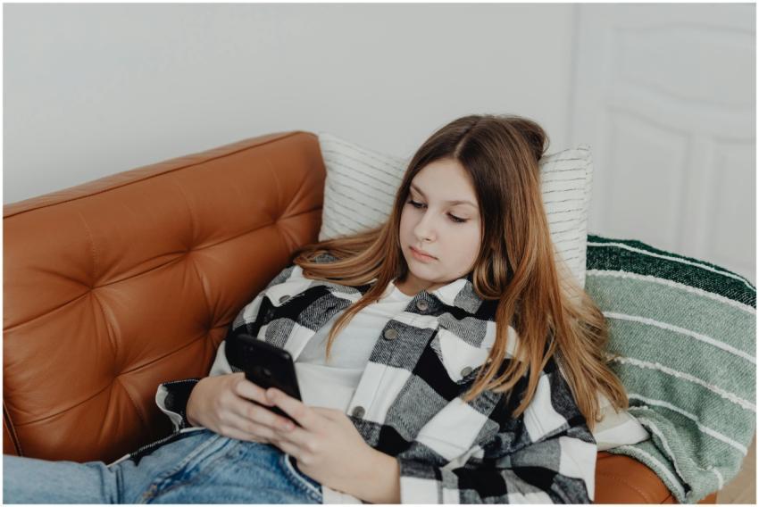 Teen girl lying on sofa using smartphone, enjoying