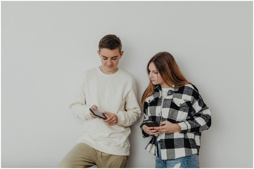 Teenage boy and girl using smartphones while leani