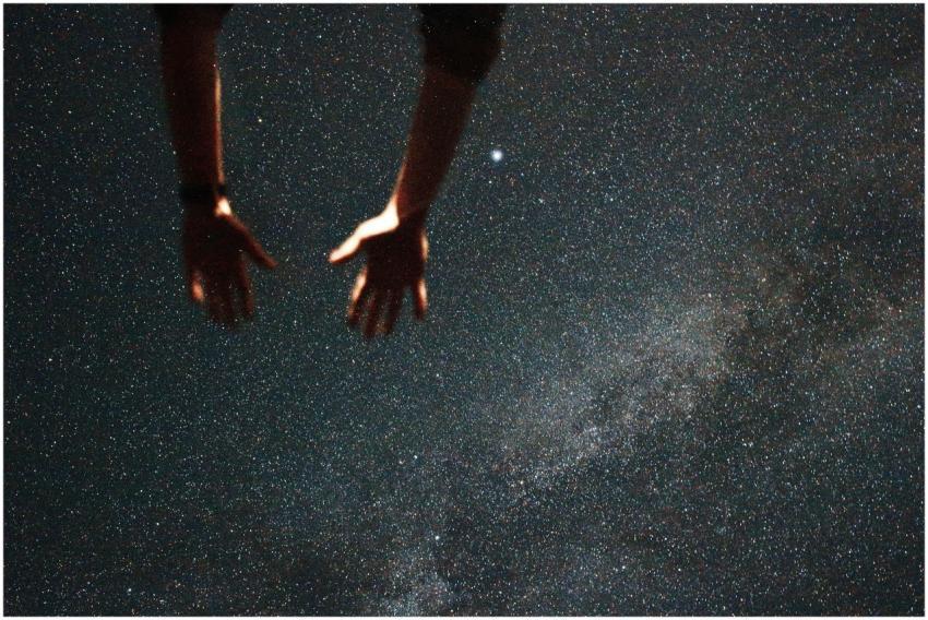 Silhouetted hands reaching towards the starry nigh