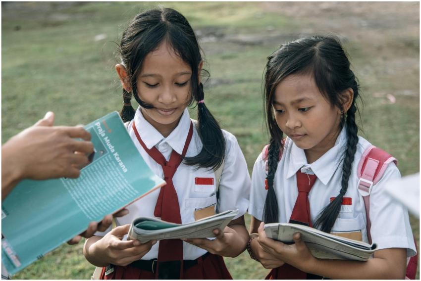 Two young girls in school uniforms reading outdoor