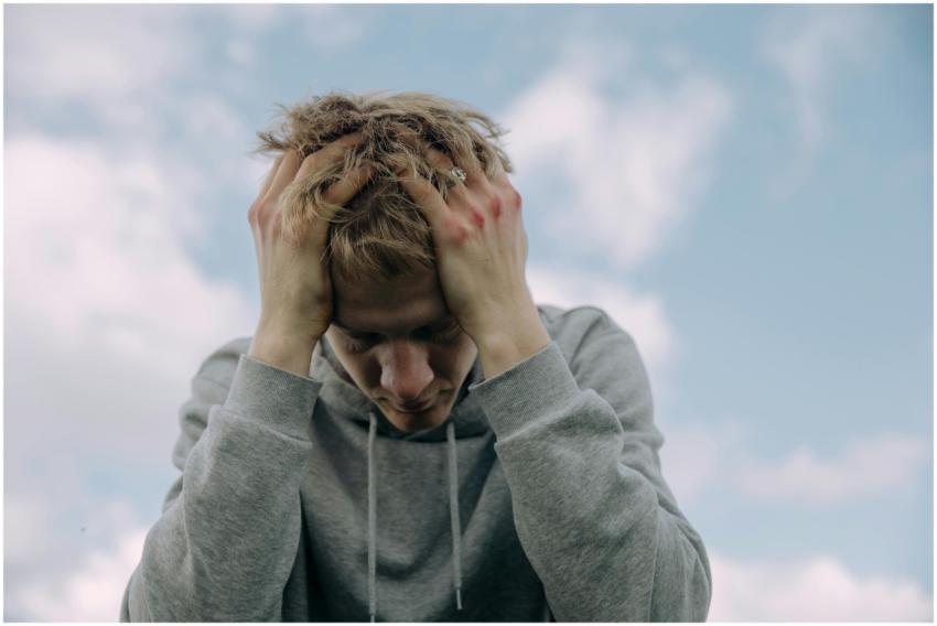 Young man in gray hoodie holds head in frustration