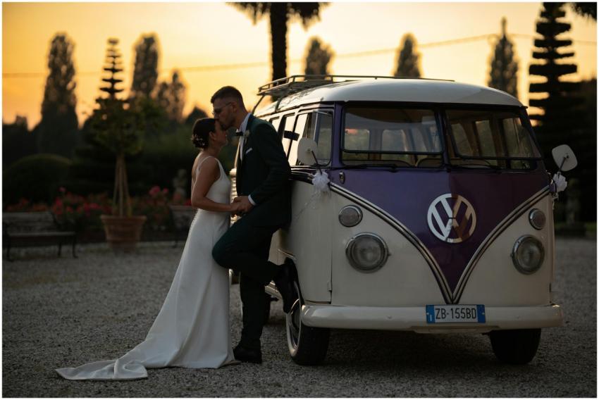 Newlyweds embrace by a vintage VW bus at sunset in
